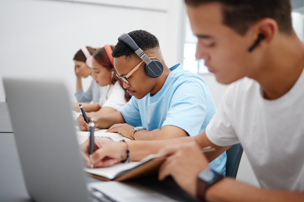 Students at university study, writing and research for a exam or project with headphones for podcas